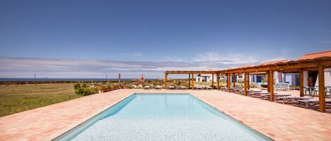 Ein rechteckiger Pool mit klarem Wasser, umgeben von einer gefliesten Terrasse und einer Holzpergola.
