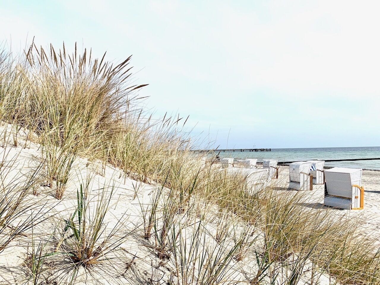 A beach with sand dunes, a pier in the background, and beach chairs.