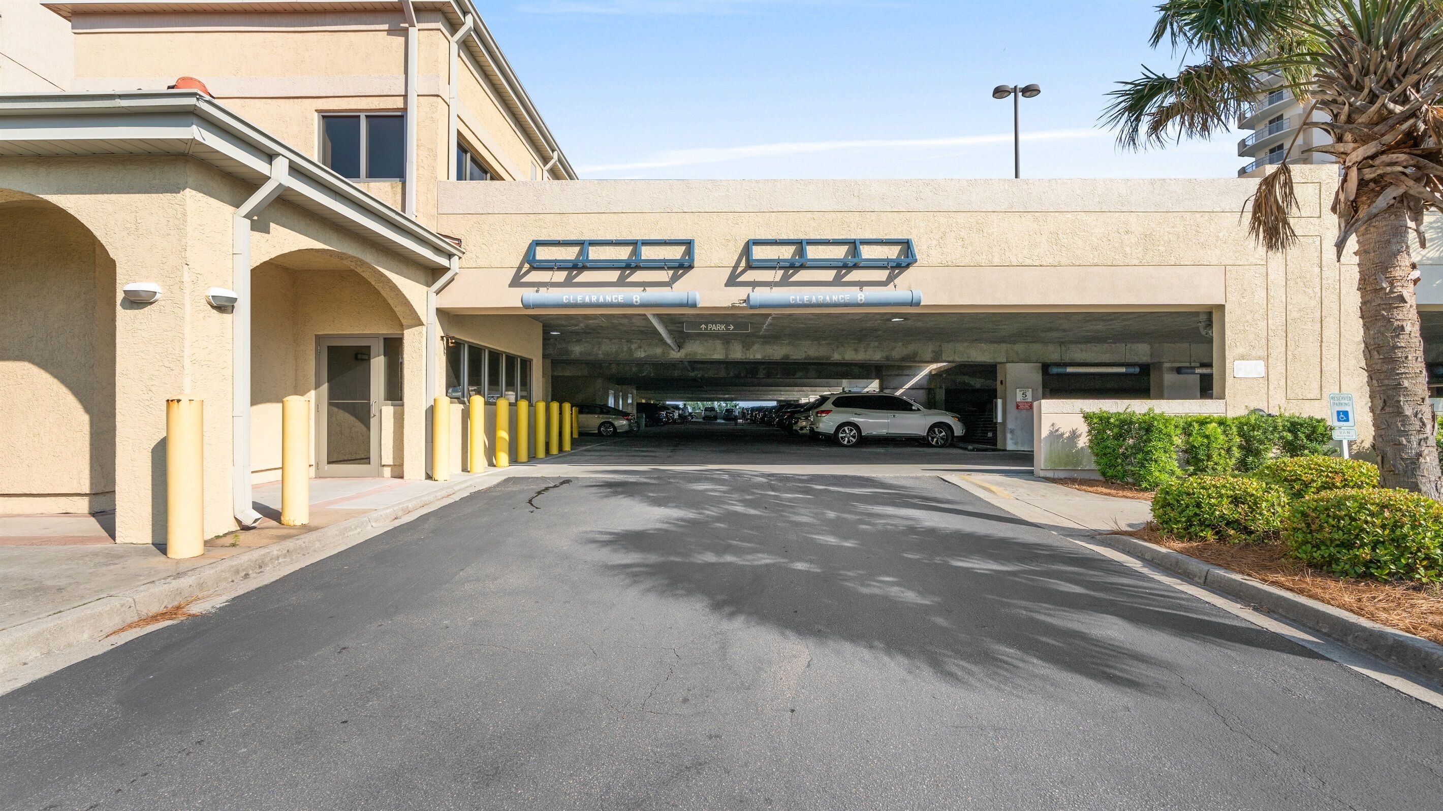 A parking garage entrance with clear signage, bollards, and a palm tree.