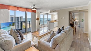 A spacious living room with a large sofa, a coffee table, and a view of the ocean through large windows. - Brighton 1803 2 Br Oceanview in Kingston w/Pool (Myrtle Beach)