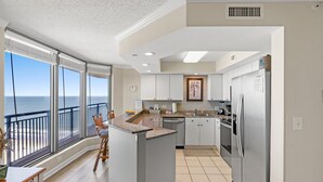 A modern kitchen with a view of the ocean, featuring a large island, stainless steel appliances, and a dining area with a view. - Brighton 1803 2 Br Oceanview in Kingston w/Pool (Myrtle Beach)