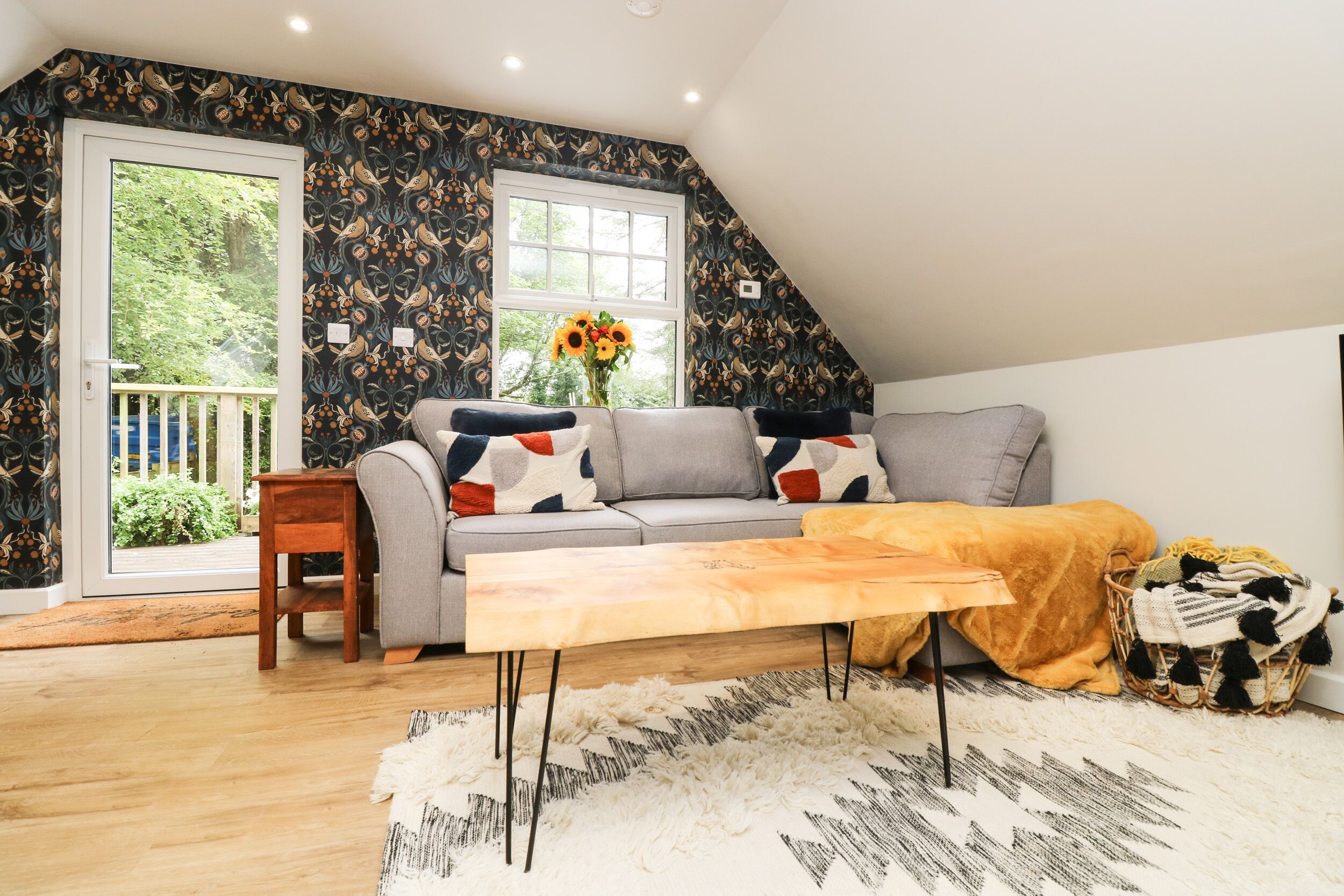 A cozy living room with a grey sofa, a wooden coffee table, and a patterned wall.