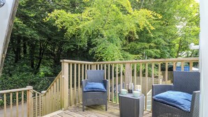 En terrasse med fletningsmøbler og gelænder i træ, omgivet af frodig vegetation.