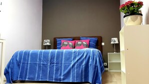 Un dormitori amb un llit, dues làmpades de nit, una tauleta de nit, un armari i una planta en test.