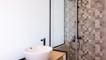 Un bany modern amb un gran lavabo blanc de disseny, un espai de banyera amb portes de vidre i parets revestides de rajoles amb disseny.