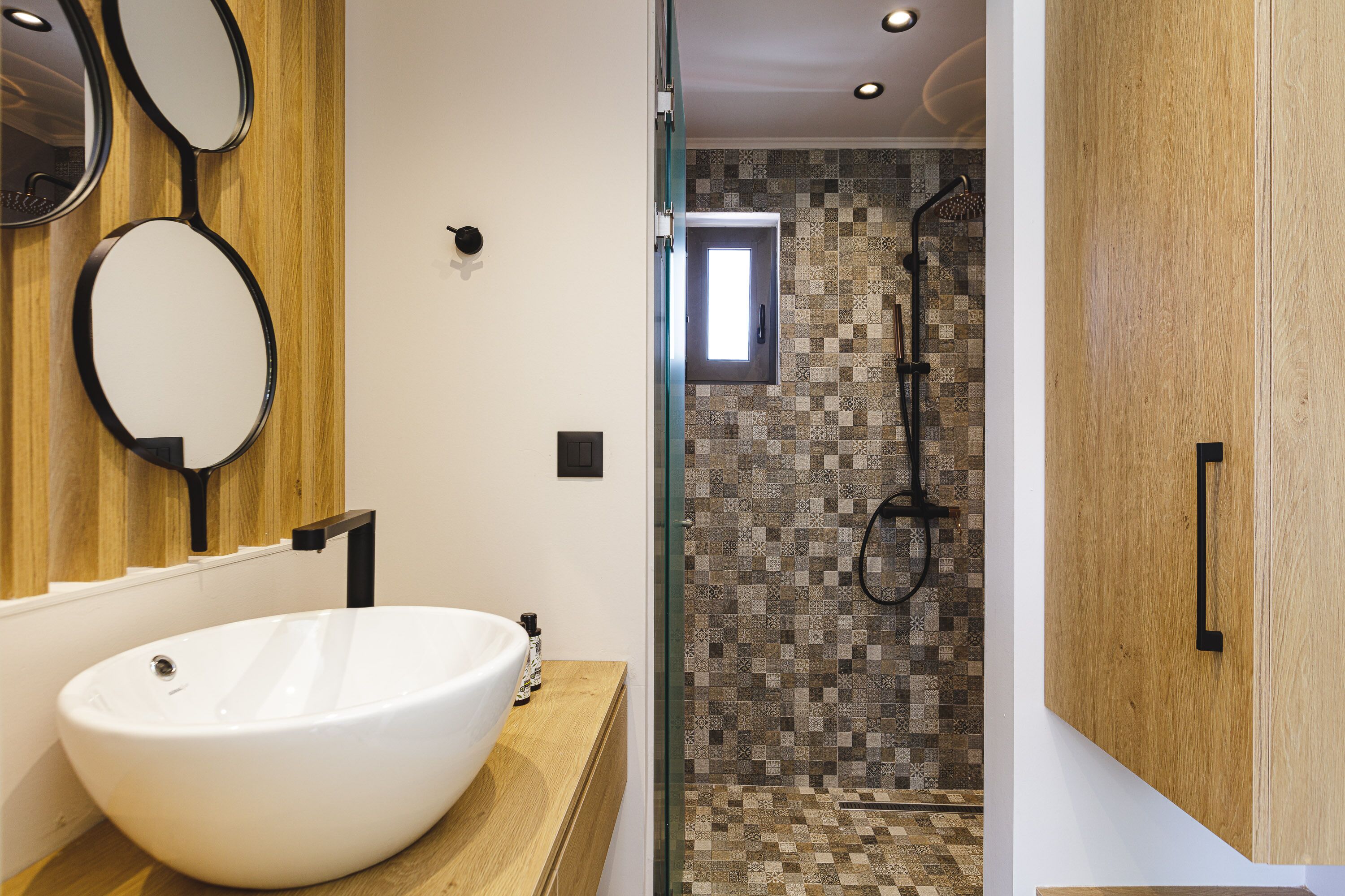 A modern bathroom with a large white sink, wooden vanity, and a shower area with patterned tiles.