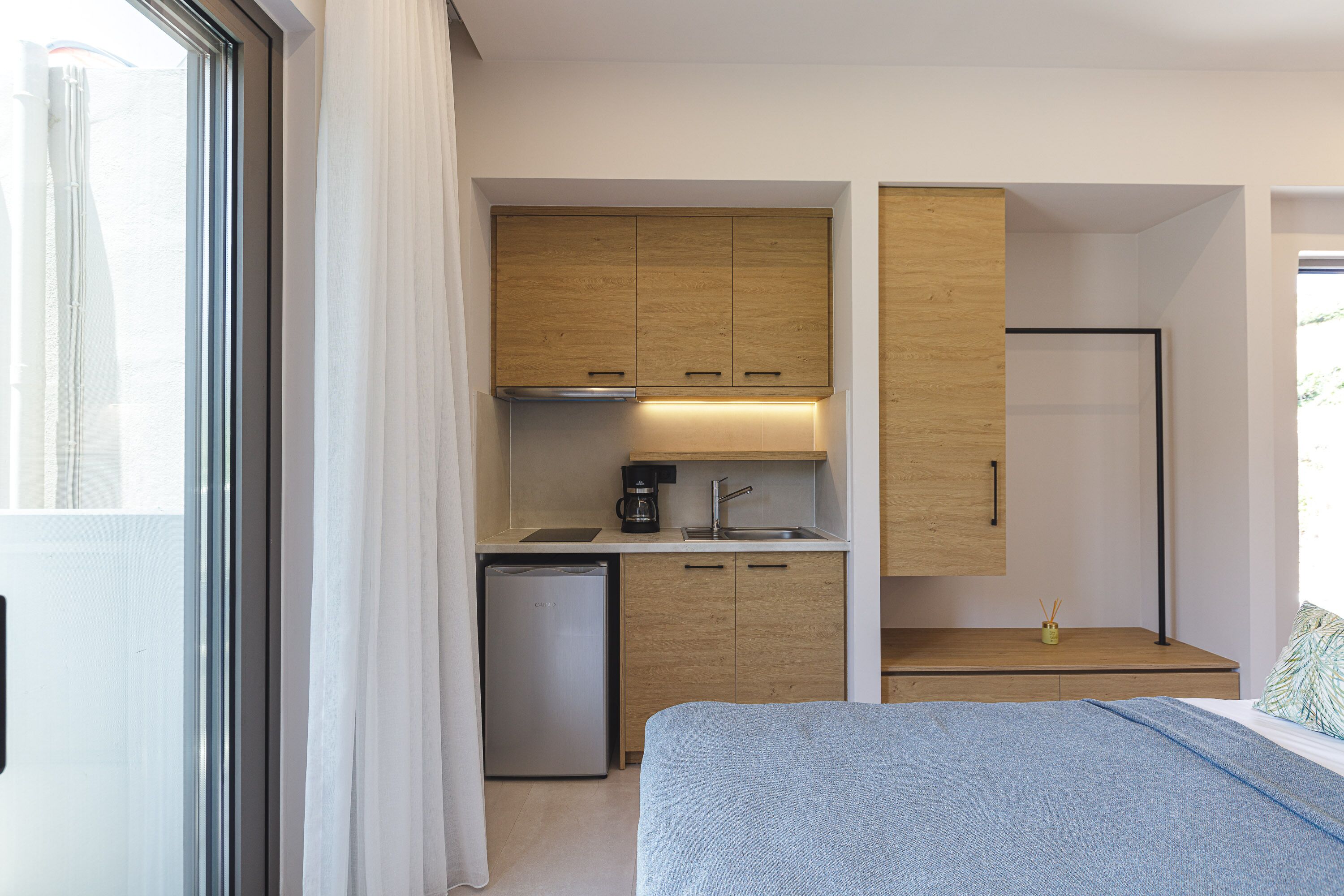 A compact hotel room with a kitchenette, a bed, and a shower area.