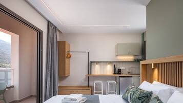Quarto de hotel moderno com cama, pequena cozinha, varanda e vista para o exterior.