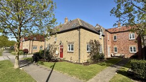 Une maison traditionnelle en briques avec une porte rouge, un petit jardin et un chemin pavé.