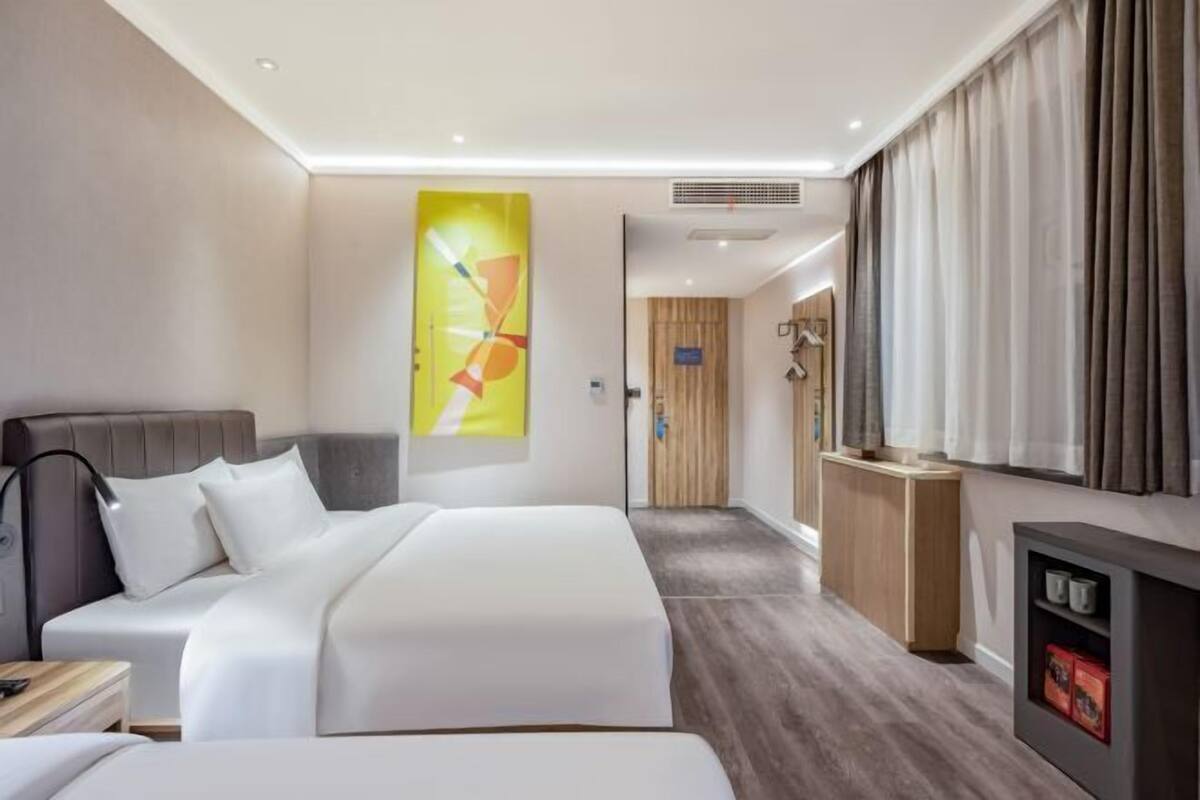 A hotel room with two beds, a large abstract painting, a wooden wardrobe, a TV, and a small shelf with items.