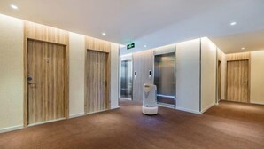 A modern hotel hallway with wooden paneling, a carpeted floor, and a robotic vacuum cleaner. - HanTing Premium Beijing South Railway Station Jiaomen East Subway Station Hotel (Beijing)