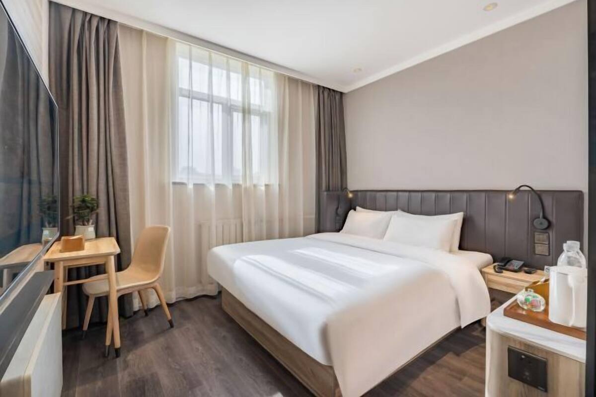 A hotel room with a bed, a desk, a chair, a TV, and a window with curtains.