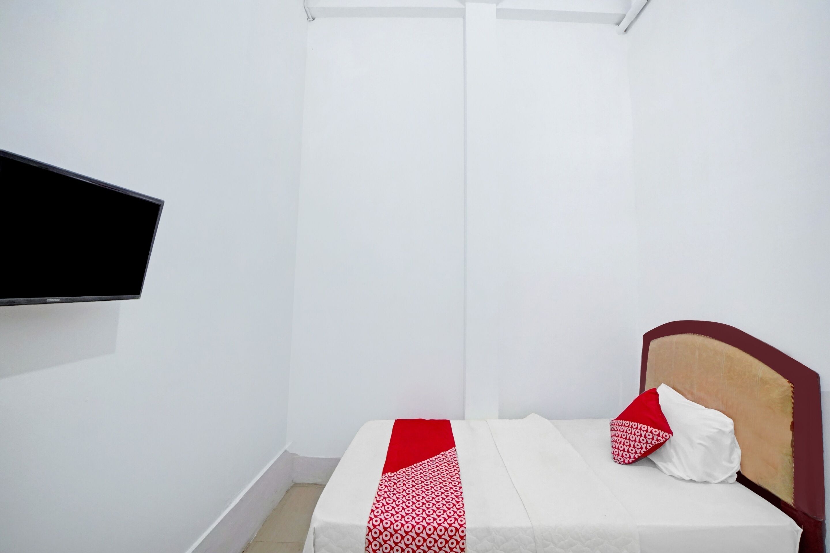 Ein kleines, aufgeräumtes Schlafzimmer mit einem Einzelbett, einem an der Wand befestigten Flachbildfernseher und einem schlichten, klaren Design.
