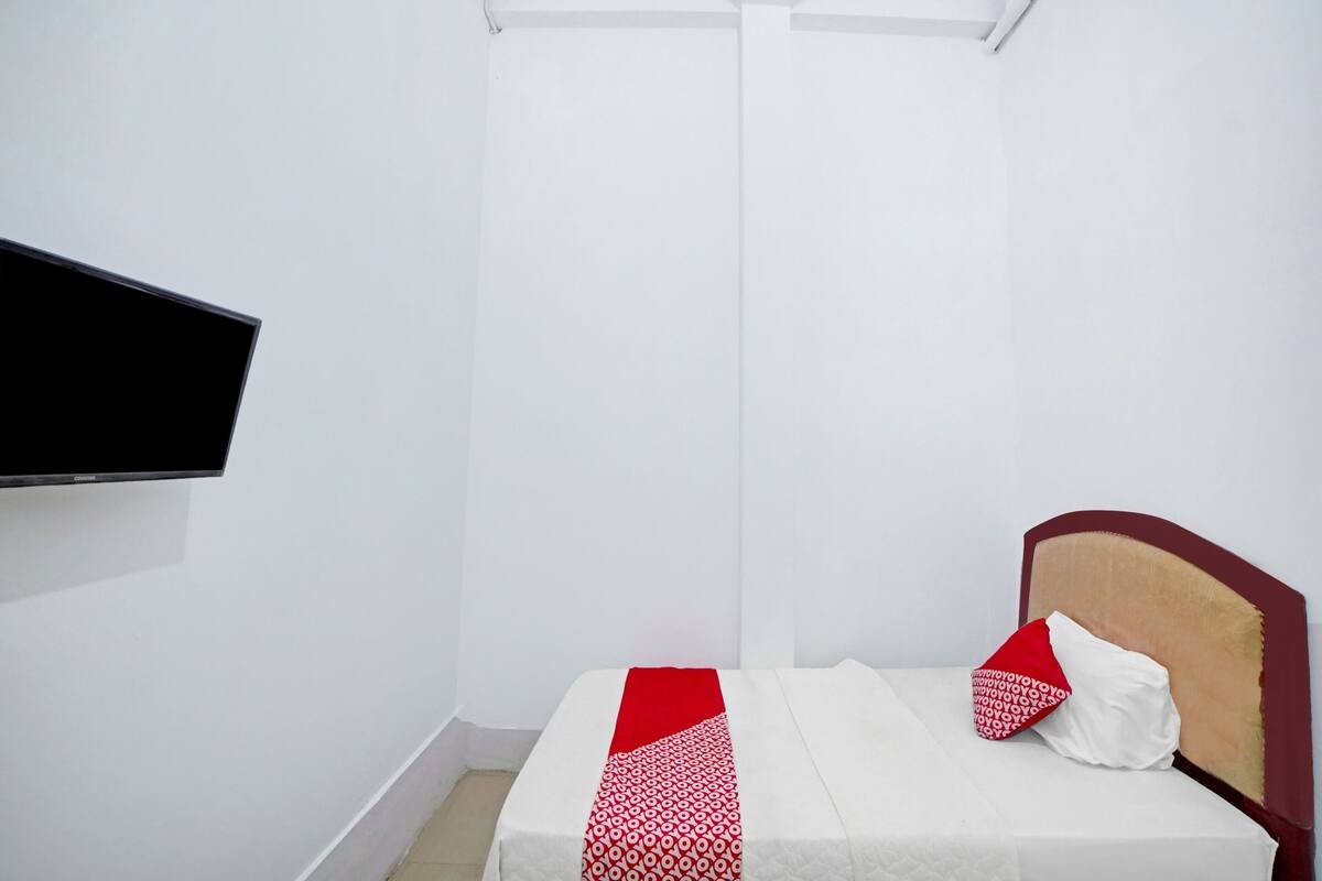 Une petite chambre à coucher, bien aménagée, avec un lit simple, un téléviseur à écran plat fixé au mur et un design simple et épuré.