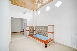A room with a bed, a bench, a clock, and a door leading to another room. - OYO 90387 Sepakat Guest House (Medan)