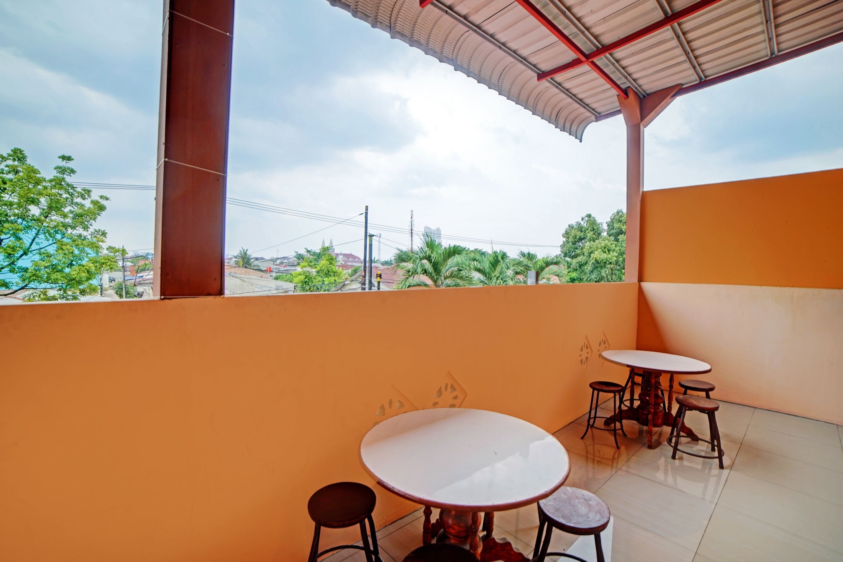 A balcony with two round tables and stools, a tiled floor, and a view of greenery and buildings in the distance.