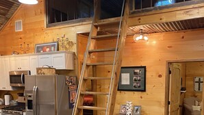 Una cocina rústica con paredes de madera, un refrigerador de acero inoxidable, una estufa y una escalera de madera que conduce a un altillo.