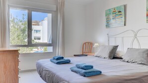 A bedroom with a bed, a chair, a nightstand, and a window with curtains. - First floor apartment in Bellresguard complex, with pool, near the beach (Puerto Pollensa)