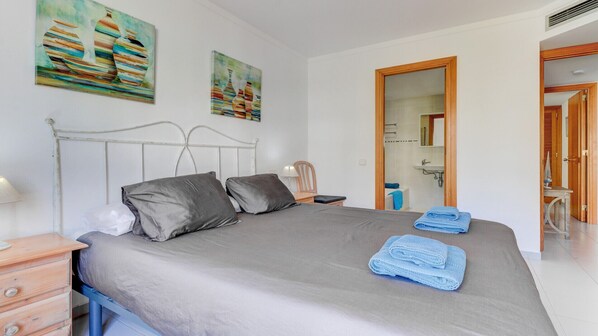 A bedroom with a bed, pillows, a nightstand, a lamp, and artwork on the wall. - First floor apartment in Bellresguard complex, with pool, near the beach (Puerto Pollensa)