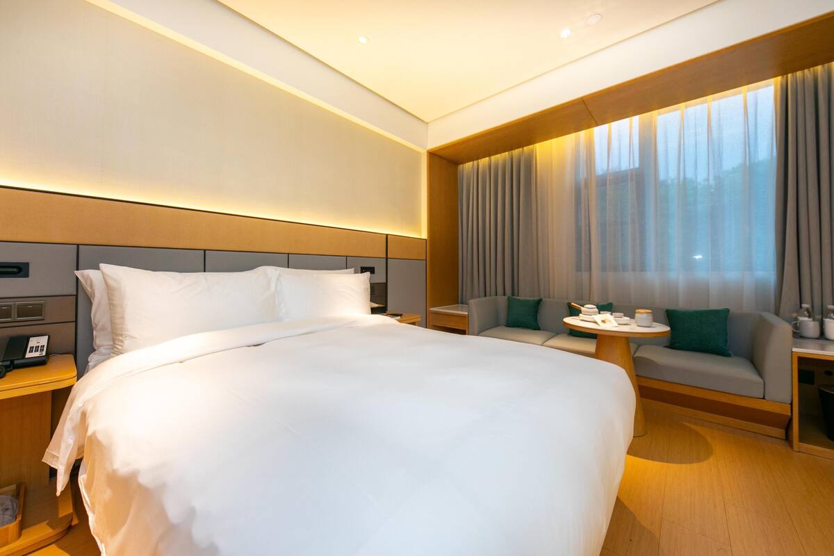 Une chambre d’hôtel avec un grand lit, un canapé, une petite table et une fenêtre avec des rideaux.