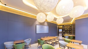 A modern library with round tables, green chairs, and a large bookshelf.
