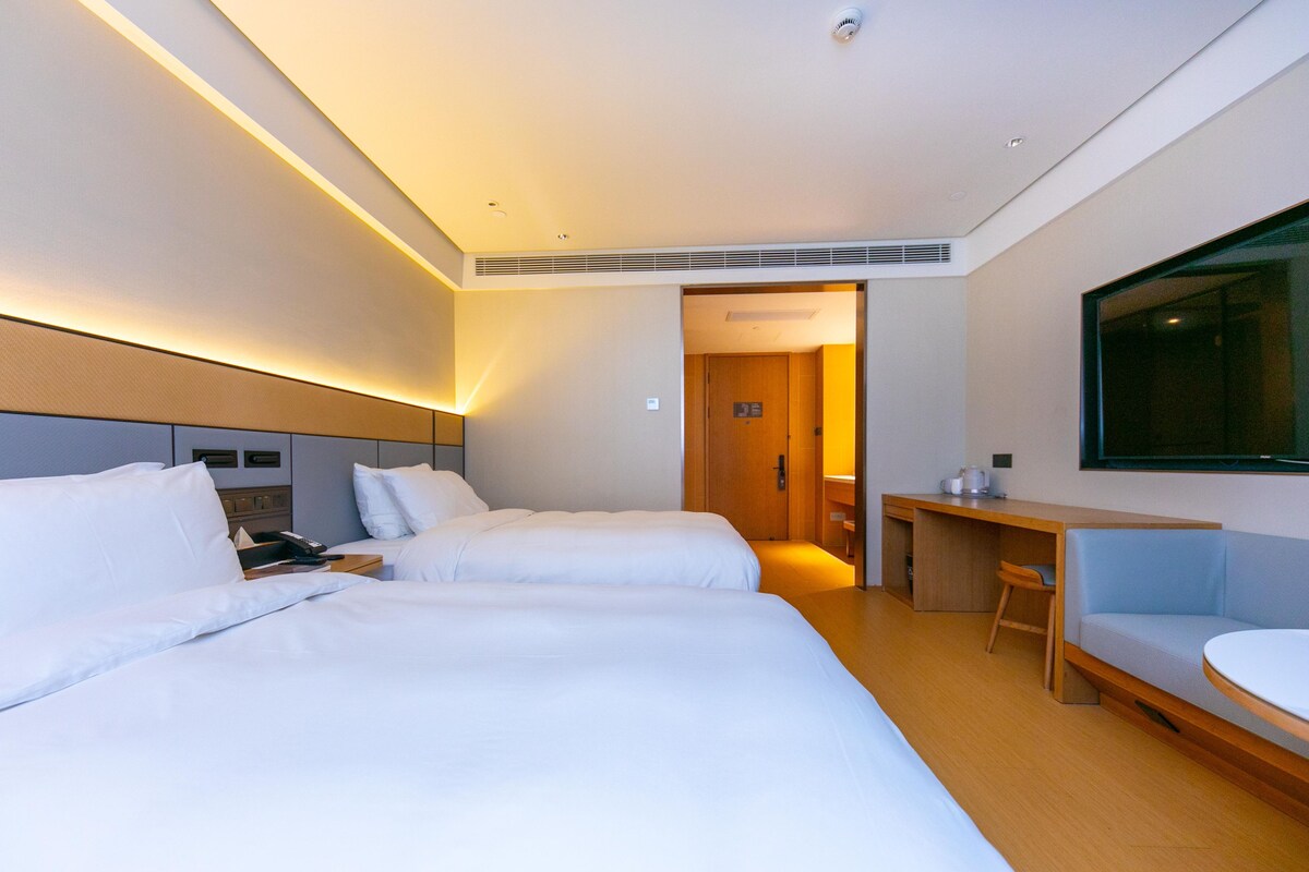 A hotel room with two beds, a desk, a chair, a TV, and a bathroom door.