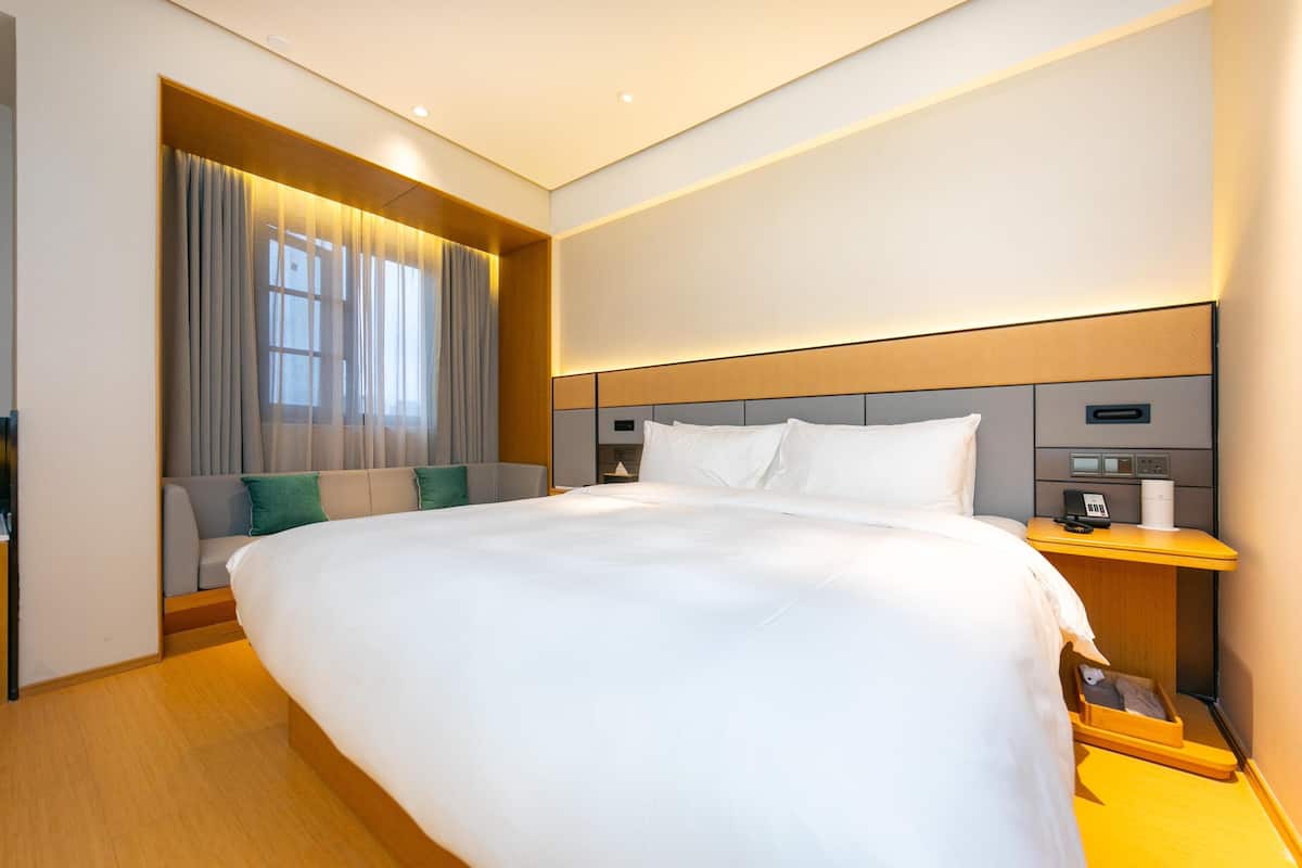 Une chambre d’hôtel moderne avec un grand lit, une table de chevet avec un téléphone et une lampe, et une fenêtre avec des rideaux.