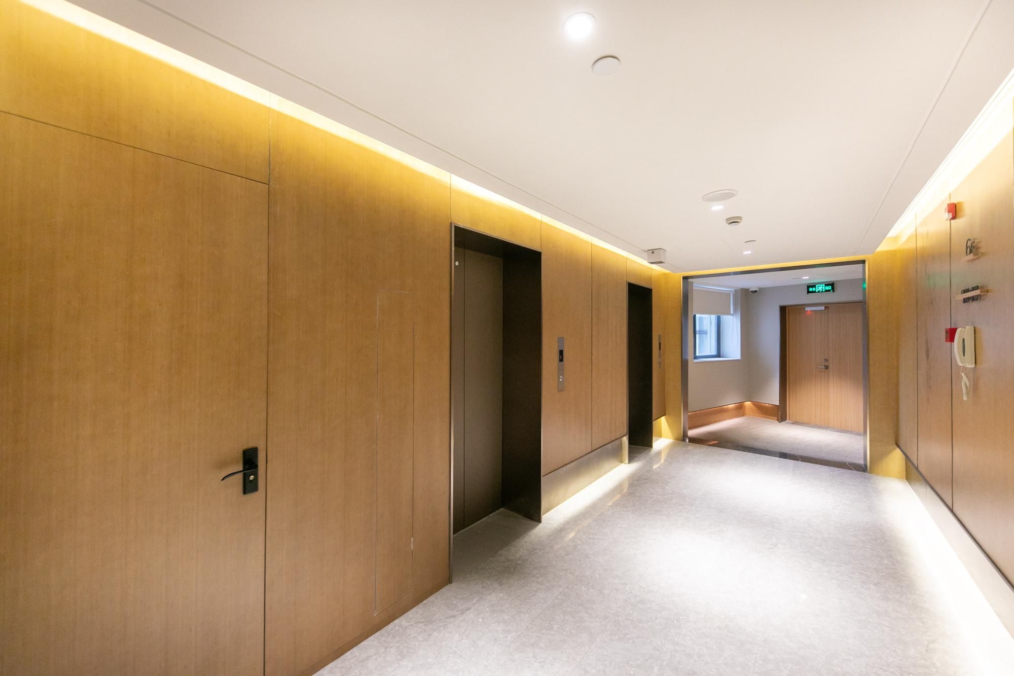 Corredor moderno de hotel com painéis de madeira, iluminação embutida e design limpo e minimalista.