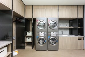 A modern laundry room with two stacked washing machines, a sink, and wooden cabinetry. - Ji Hotel (Shanghai)