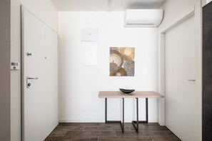 A hallway with a white door, a wall-mounted air conditioner, a framed artwork, and a small table with a bowl.