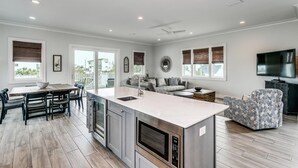 A modern kitchen with a central island, dining area with chairs, a sofa, and a TV in a living room. - Luxury Gulf View Home with Private Pool! Steps to the beach! (Pensacola Beach)