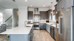 A modern kitchen with a central island, stainless steel appliances, and a herringbone tile backsplash. - Luxury Gulf View Home with Private Pool! Steps to the beach! (Pensacola Beach)