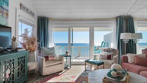A spacious living room with a large window overlooking the sea, a cozy seating area with a coffee table, and a decorative cabinet. - 30A condo. Private beach. Incredible view! (Seacrest)