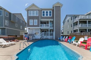 A swimming pool with a deck area, lounge chairs, and a multi-story building with balconies. - High Cotton - Old Nags Head Place, Ocean View, 325 Yds to Beach, Elevator, Pool, Hot Tub, Tiki Bar (Nags Head)