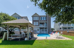 A residential backyard with a pool, a covered patio, and a wooden deck.