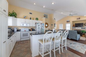 A spacious kitchen with white cabinetry, a central island with chairs, and a dining area with a gray sofa.