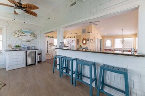 A kitchen with a central island, bar stools, and a ceiling fan. - High Cotton - Old Nags Head Place, Ocean View, 325 Yds to Beach, Elevator, Pool, Hot Tub, Tiki Bar (Nags Head)