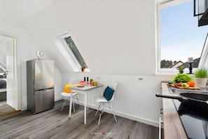 Une cuisine moderne dotée d’un réfrigérateur encastré, d’un coin repas avec une table et des chaises blanches, et d’une fenêtre offrant une vue sur l’extérieur.
