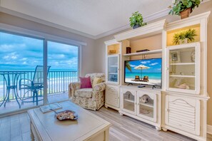 Een woonkamer met een grote televisie, een eettafel en uitzicht op de oceaan.