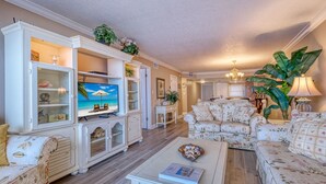 A living room with a television, floral-patterned sofas, a coffee table, and a cabinet with glass doors. - **DIRECT BEACH FRONT**GREAT LOCATION** 2 BEDROOM 2 BATH**AWESOME VIEWS** (Madeira Beach)