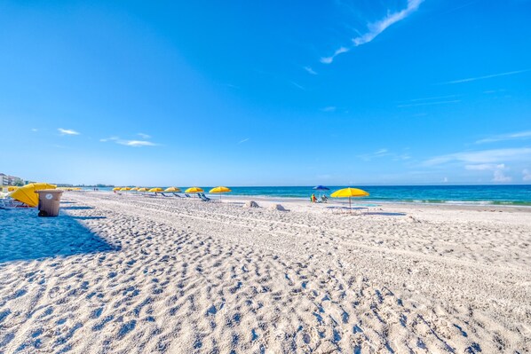 Een strand met gele parasols en een helderblauwe lucht.