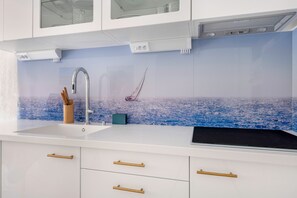 Eine moderne Küche mit weißer Arbeitsplatte, einem Edelstahlarmaturen und einer Rückwand mit einer Szene vom blauen Meer.
