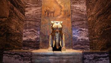 Una estatua de un elefante en un museo, con paredes de mármol y un cuadro vertical al fondo.
