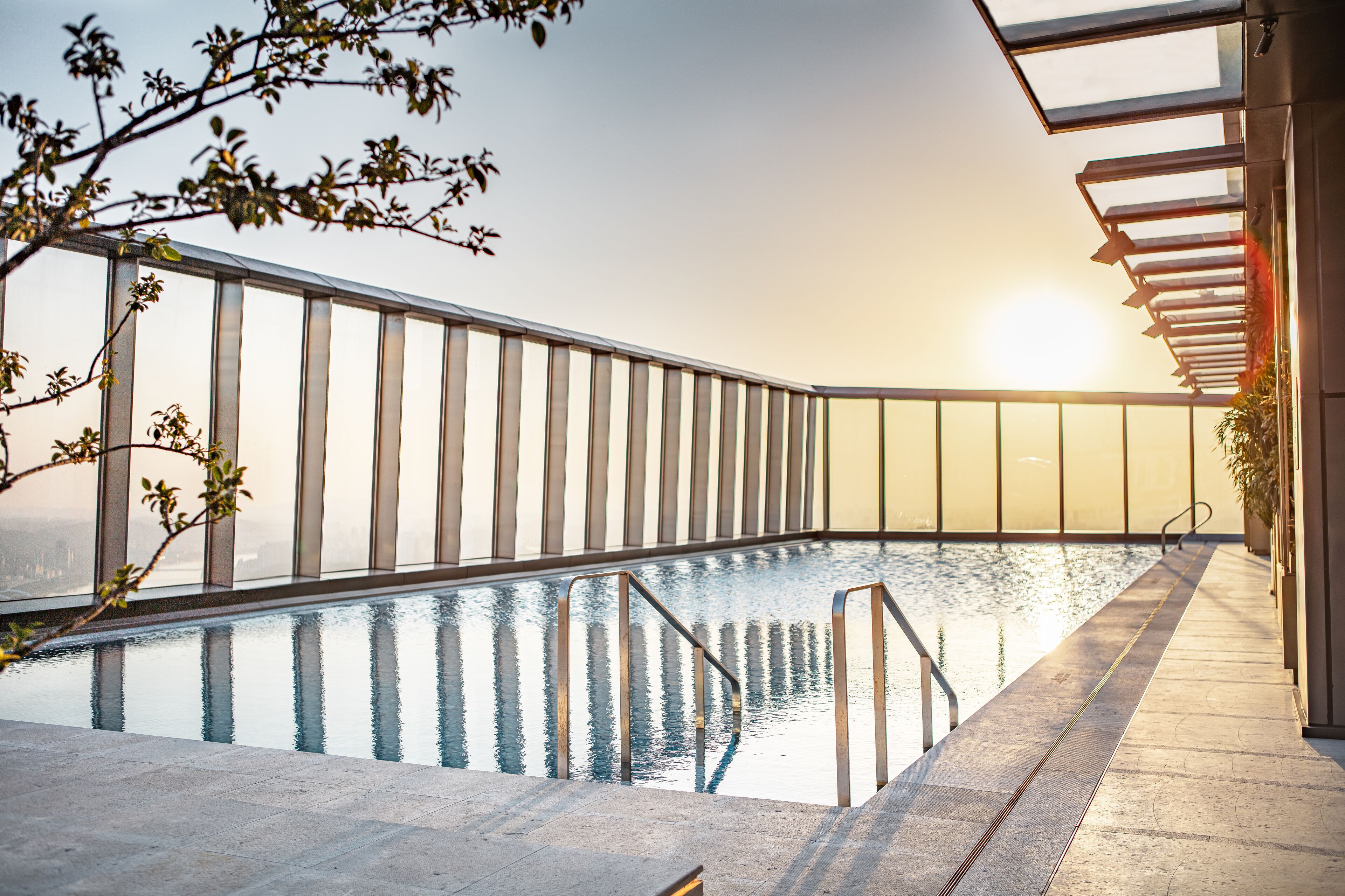 Una piscina moderna en interior con paredes de vidrio transparente, un suelo de baldosas y vistas a la silueta urbana.