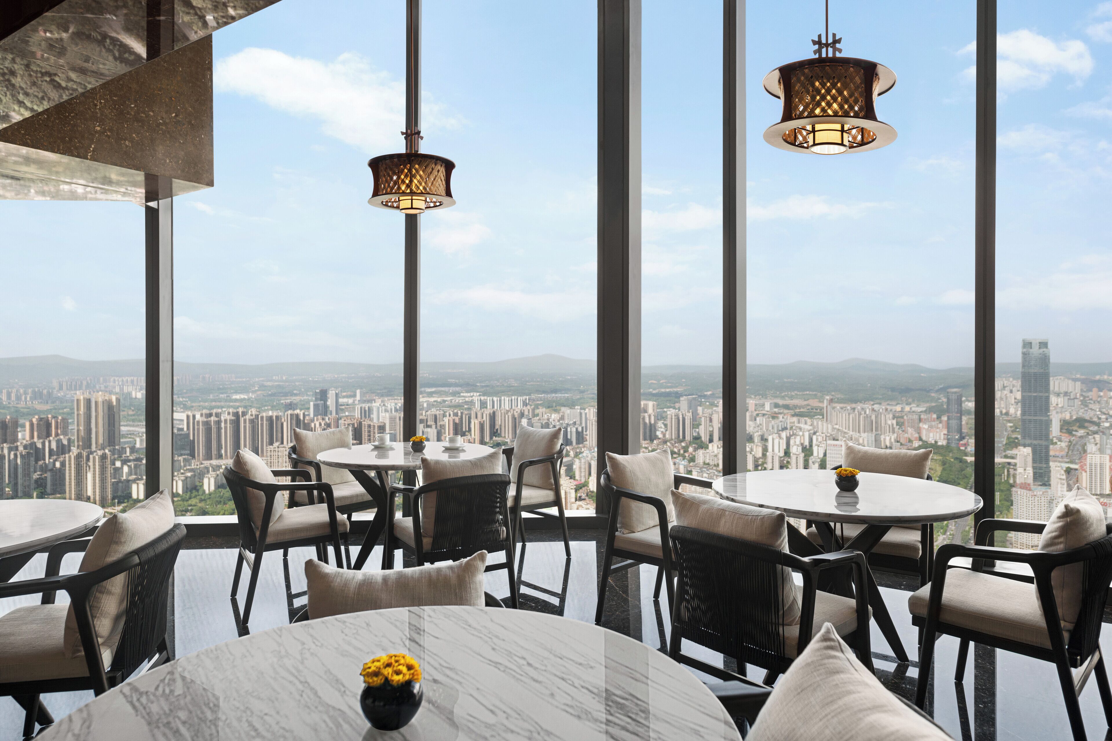 A high-rise restaurant with multiple tables and chairs, large windows offering a city view.