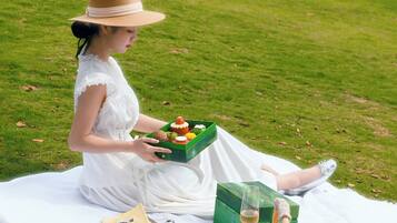 A person sitting on a blanket outdoors, holding a green box with food items.