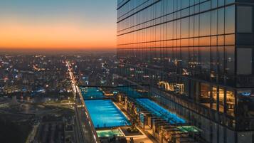 A high-rise building with a rooftop pool and lounge area, surrounded by a cityscape at dusk.
