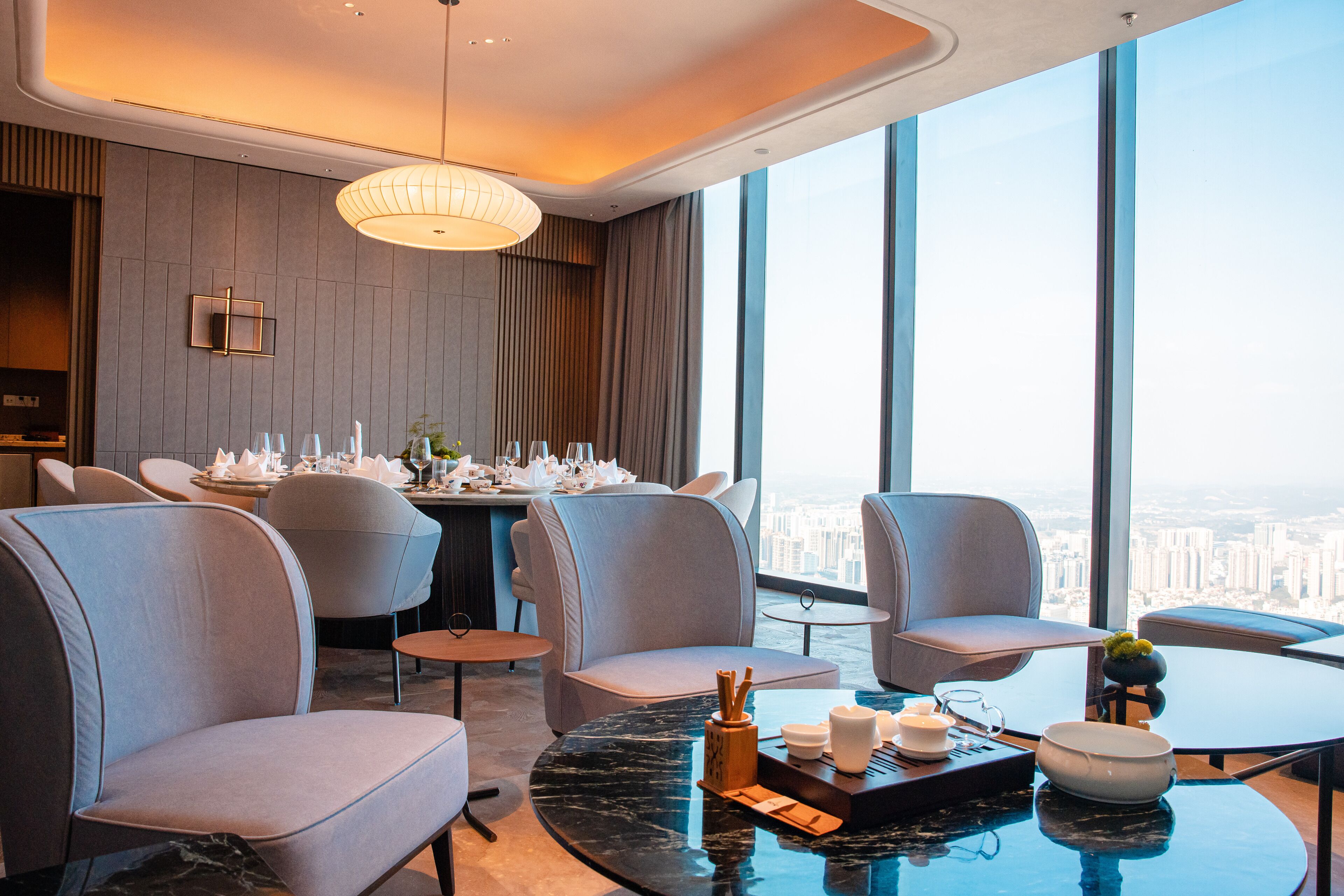 Habitación de hotel moderna con vista a la ciudad, zona de comedor con mesa preparada para cuatro personas y asientos cómodos.