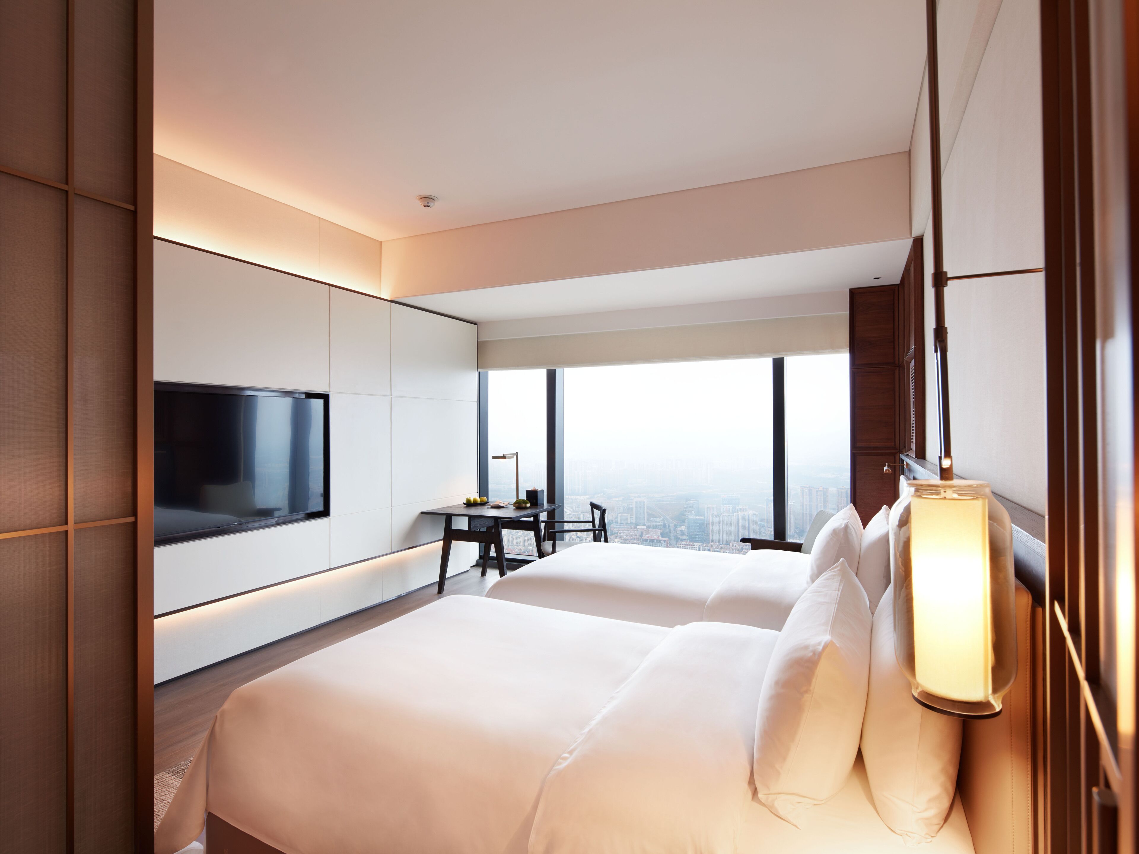 A modern hotel room with a large bed, a desk, and a TV mounted on the wall.