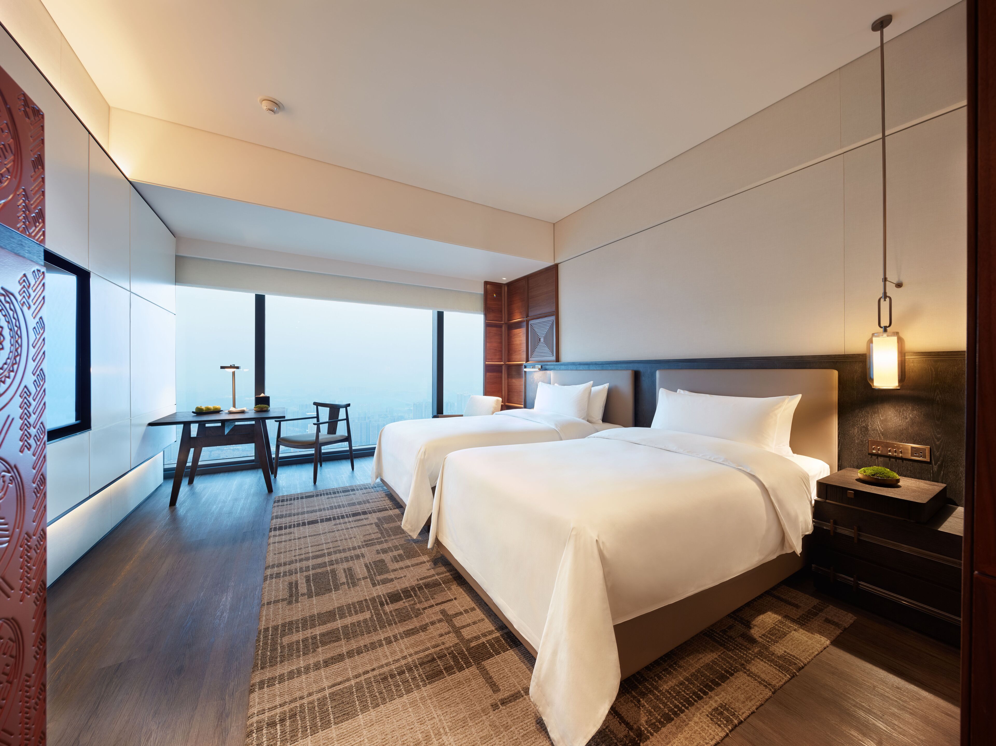 Una habitación de hotel moderna con dos camas, un escritorio y vistas a la ciudad.